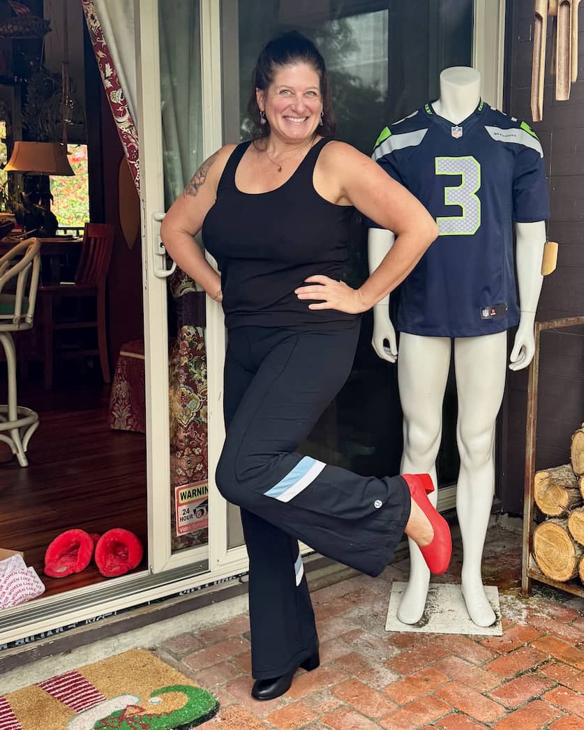 Woman posing outdoors in Lava Red and Black PIAR Performance Heels next to Seahawks jersey mannequin