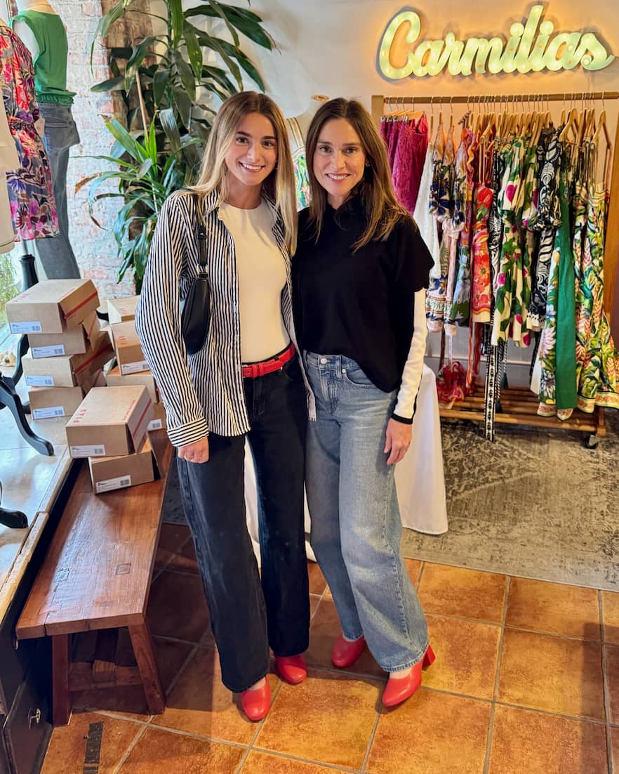 Two women wearing Lava Red PIAR Performance Heels in front of Carmilias clothing display