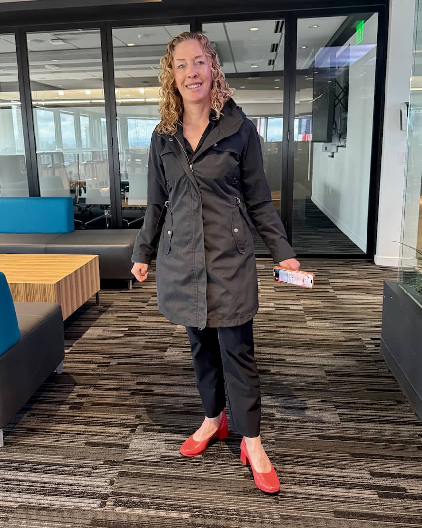 Woman in black jacket and Lava Red PIAR Performance Heels standing in office lounge