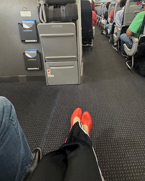 Woman seated on airplane wearing Lava Red PIAR Performance Heels and track pants