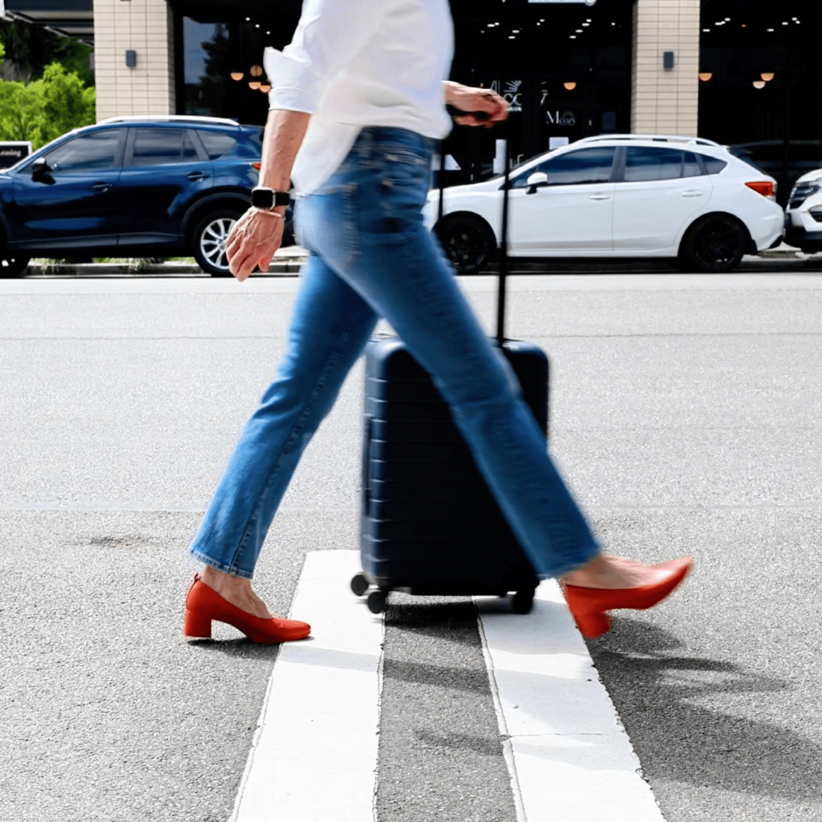 The Performance Heel by PIAR - Woman Wearing Stylish and Comfortable Black Leather Block Pumps Rolling Luggage In A Crosswalk